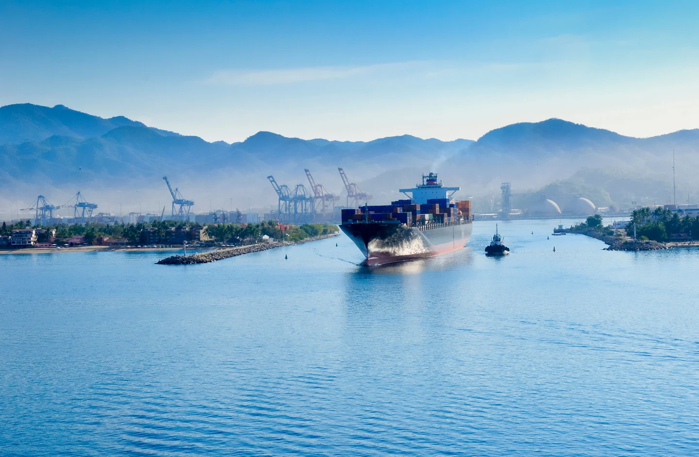 Container ship and tugboat at the Port of Manzanillo, with port infrastructure in the background