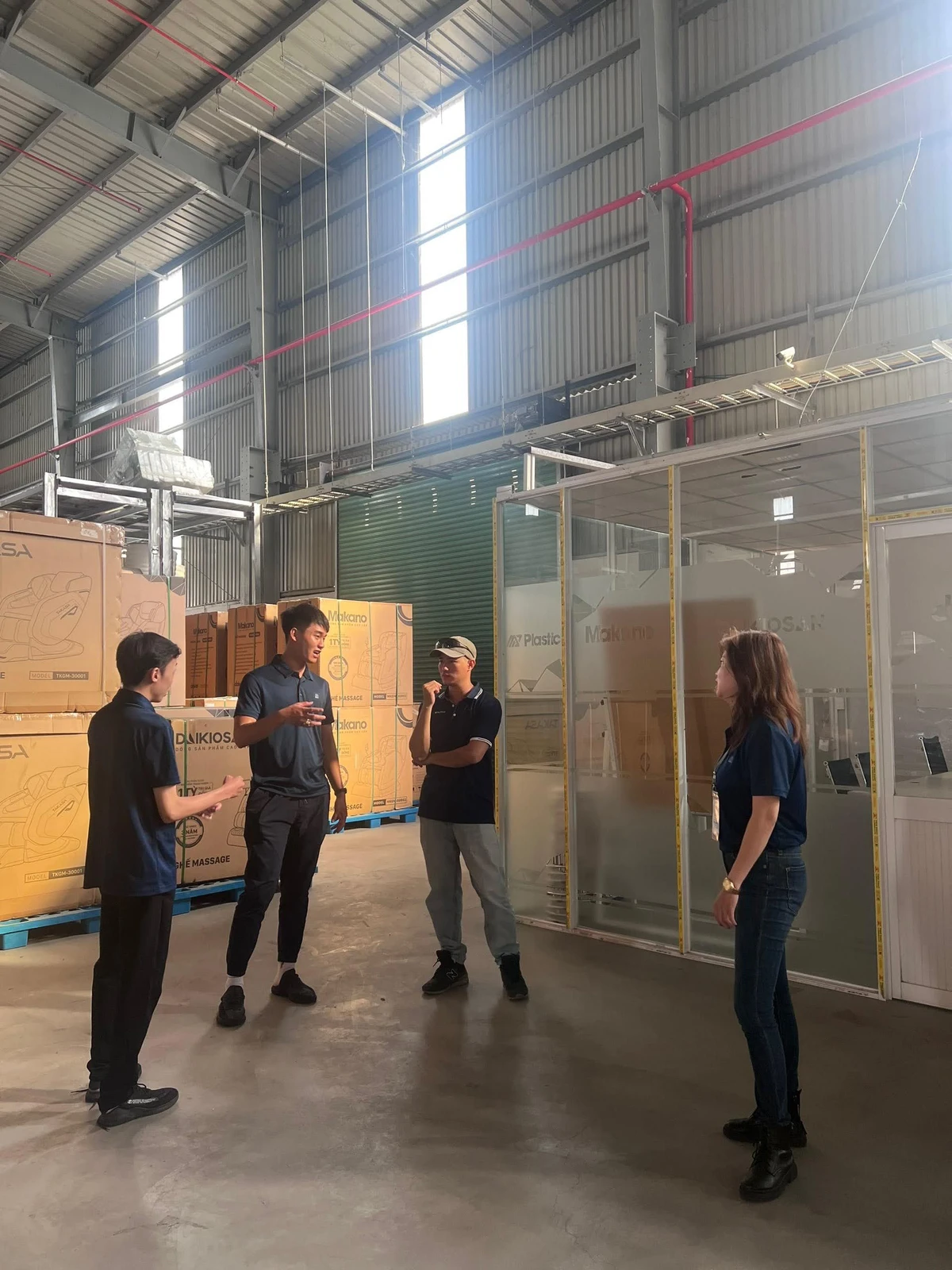 Four people talk inside an industrial warehouse beside packaged goods.